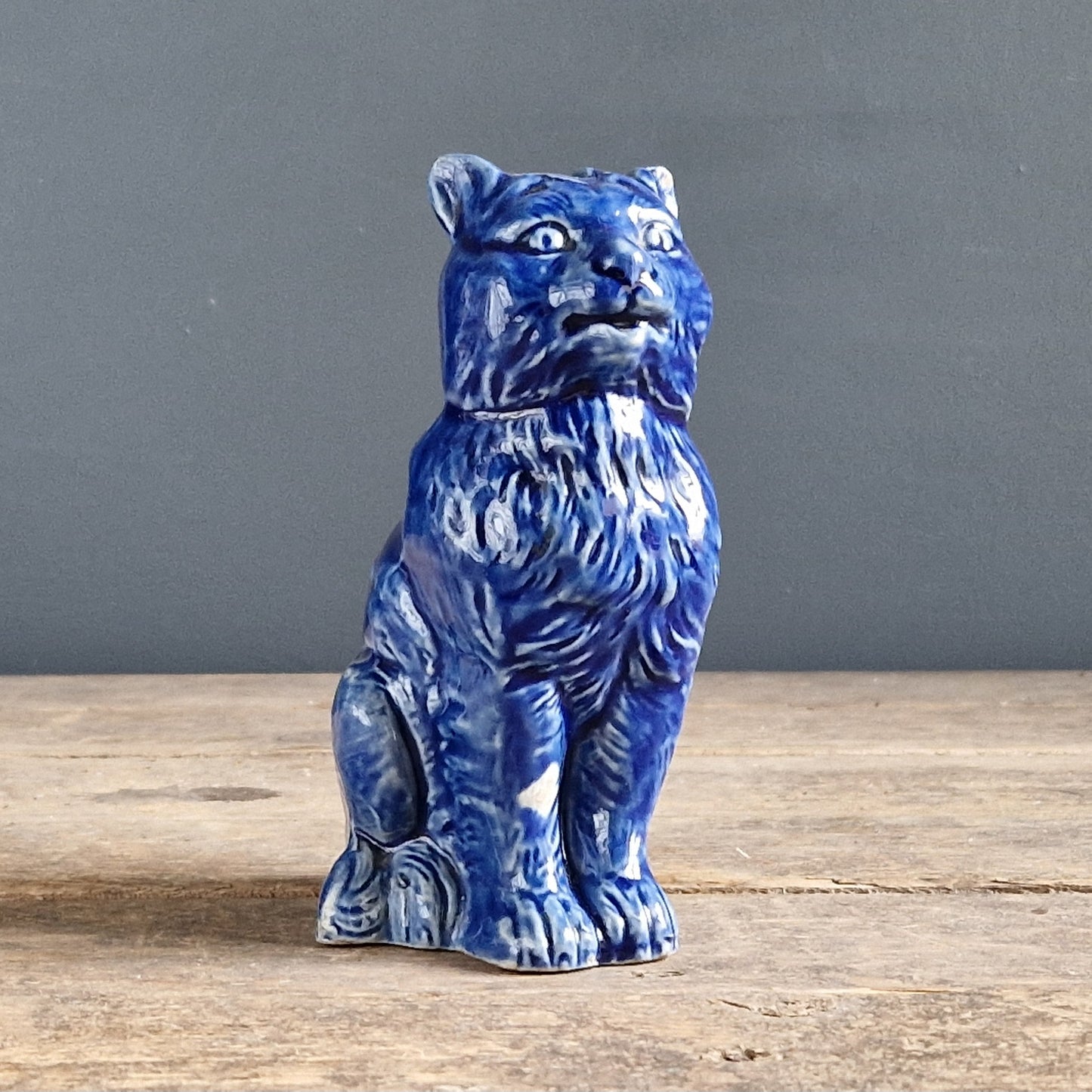 Blue ceramic cat  figurine on a wooden surface with a gray background