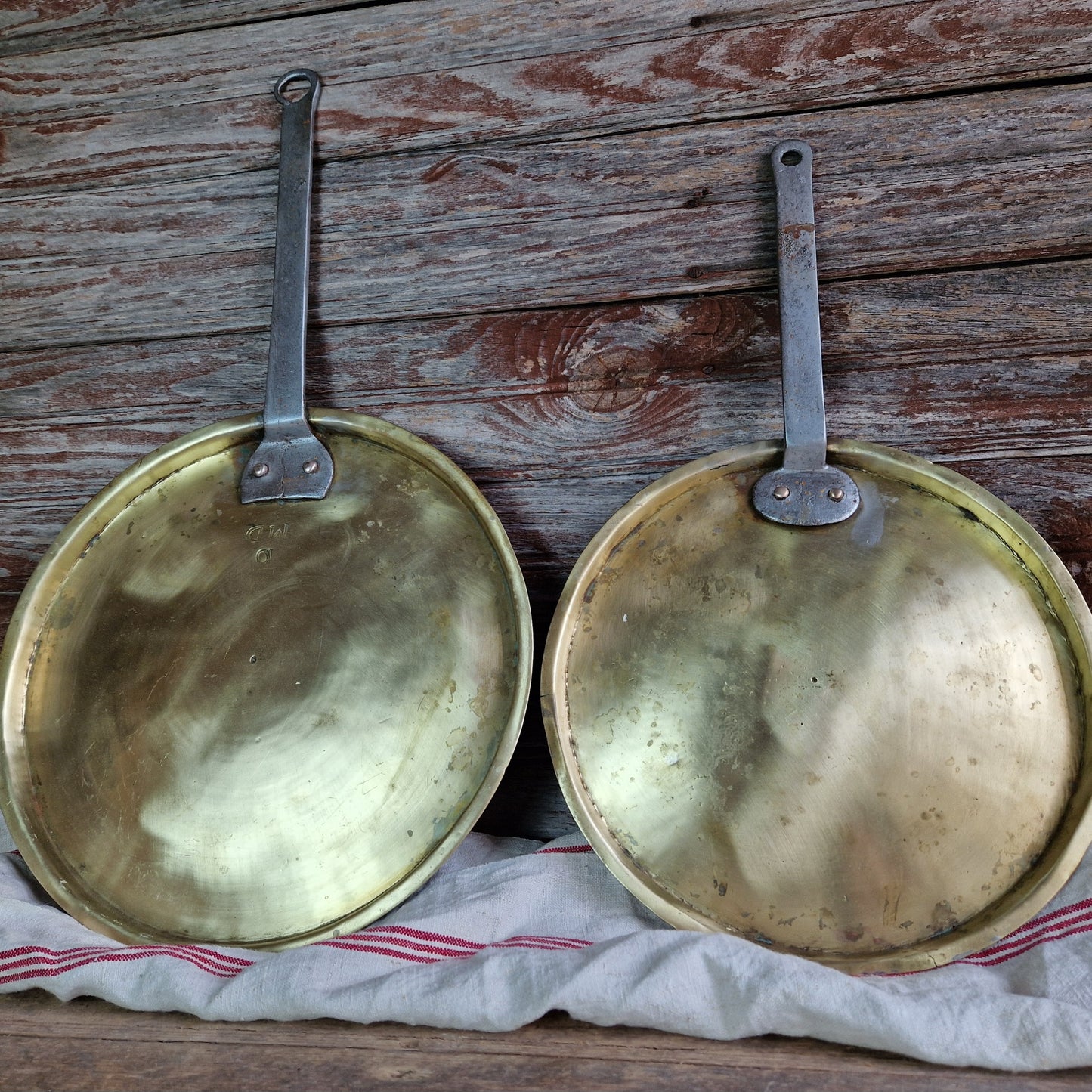 Two brass pans with handles on a wooden surface