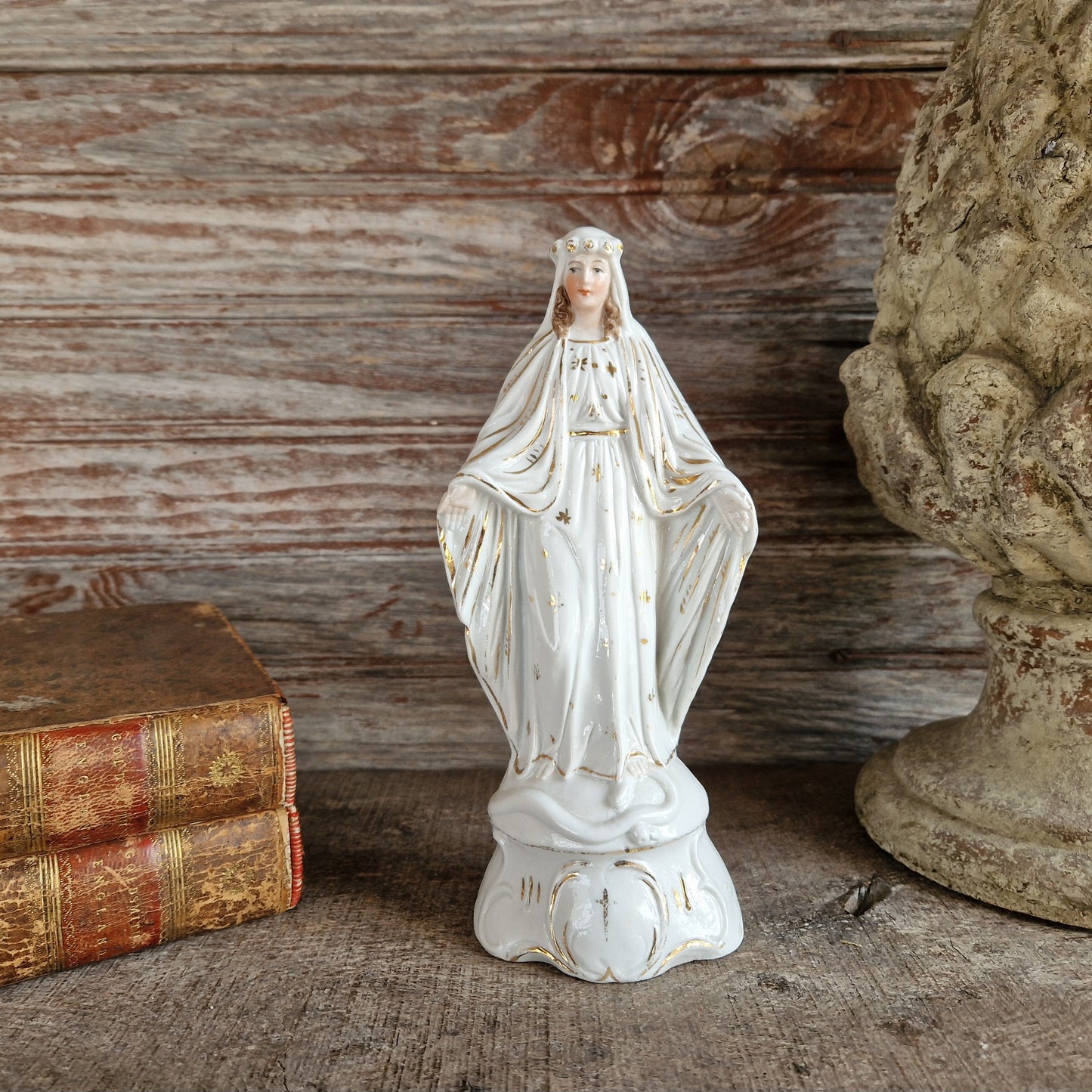 White porcelain statue of the Madonna with a wooden background and old leather books.