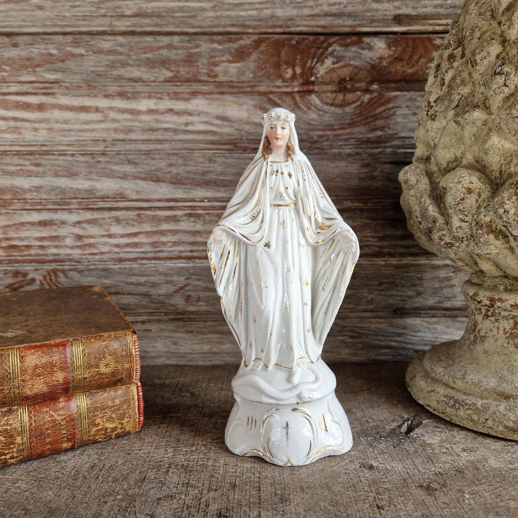 White porcelain statue of the Madonna with a wooden background and old leather books.