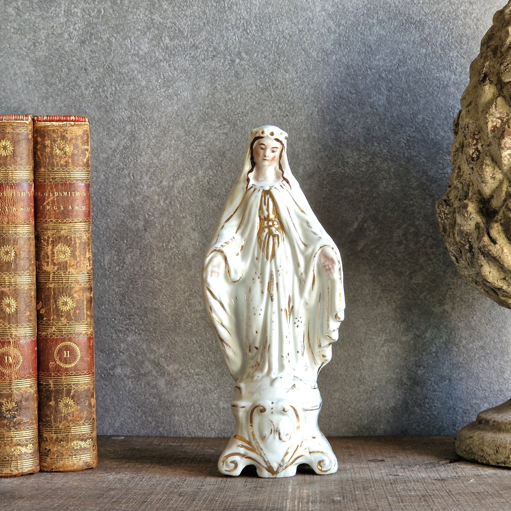 Statue of a religious figure next to two old books on a textured surface.