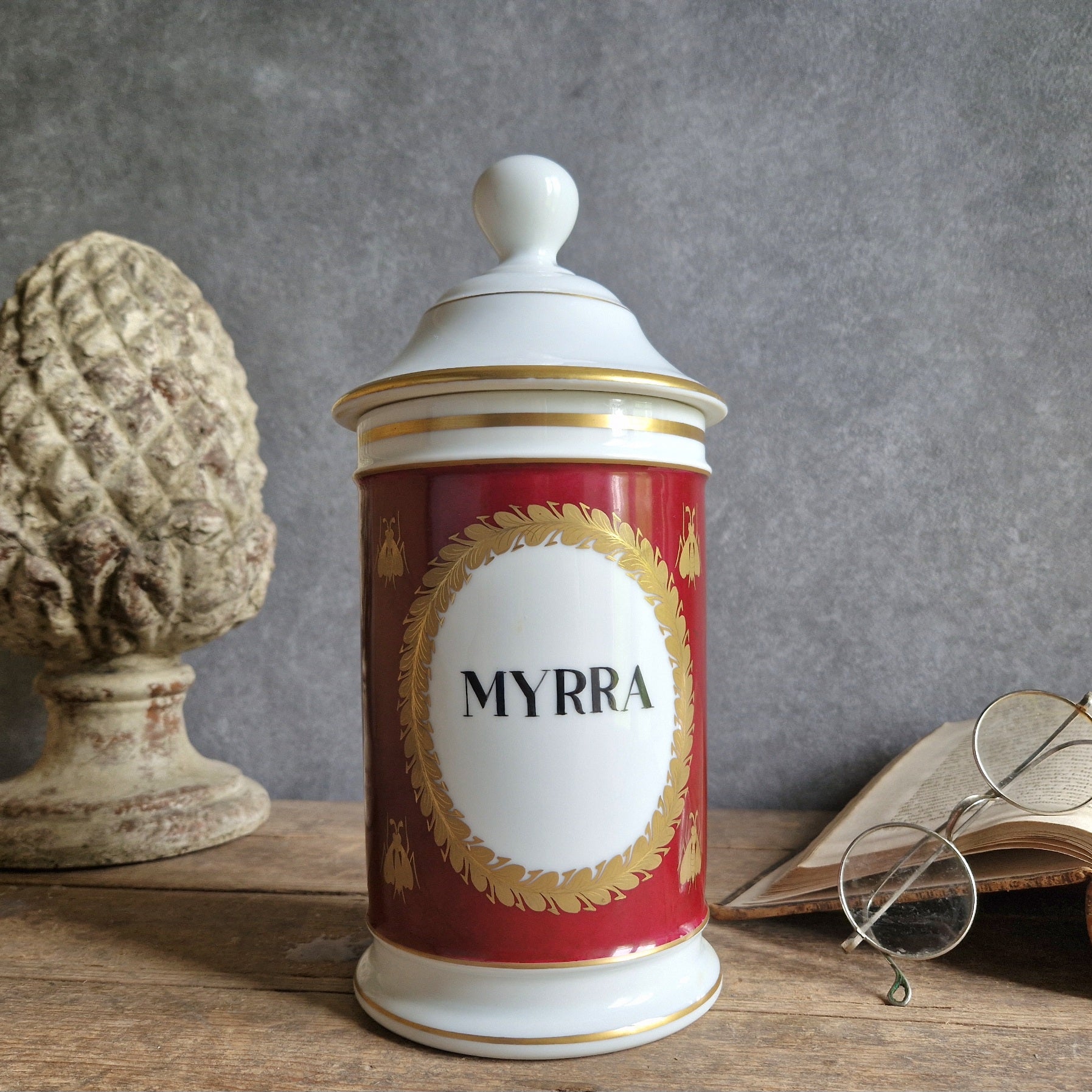Decorative jar labeled 'MYRRA' on a wooden surface with a textured gray wall background.