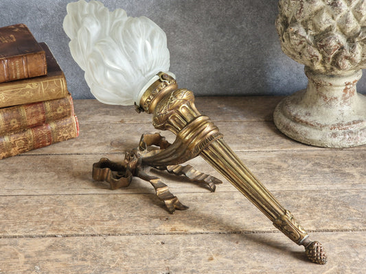 Antique bronze applique sconce with flame glass shade on a wooden background.